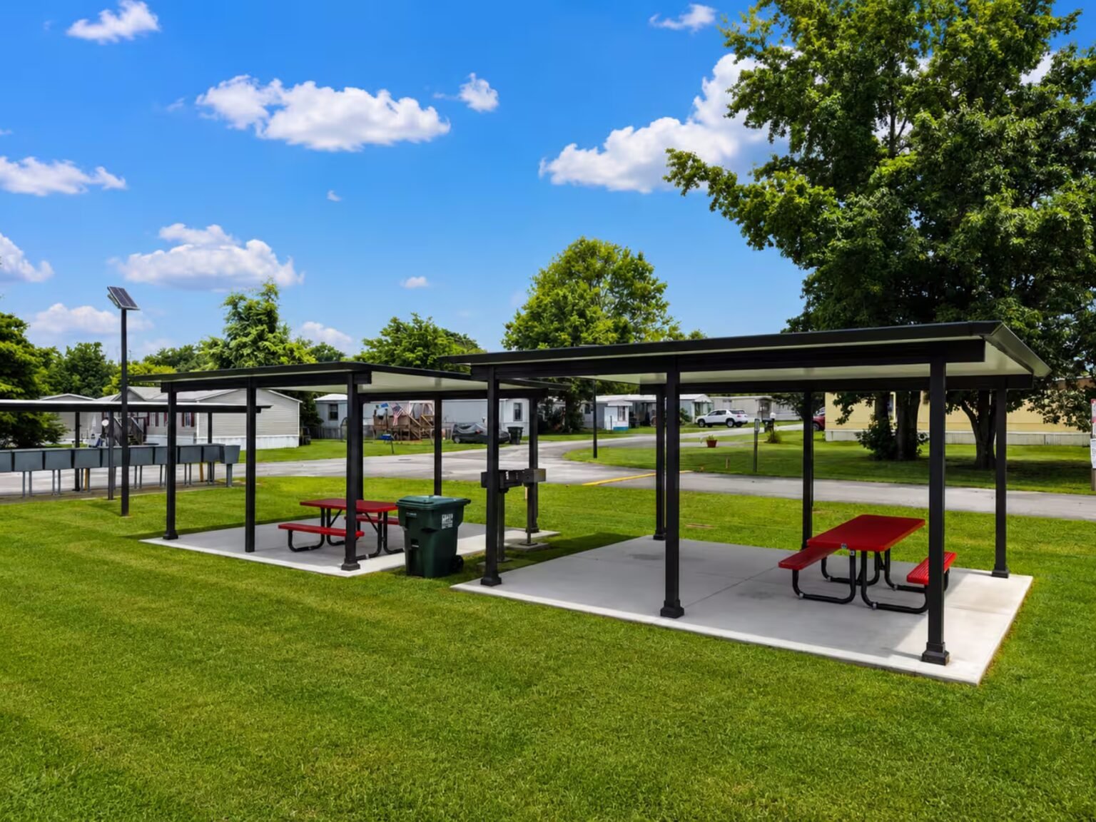 Picnic pavilion with red tables and dark roof in grassy park under partly cloudy sky