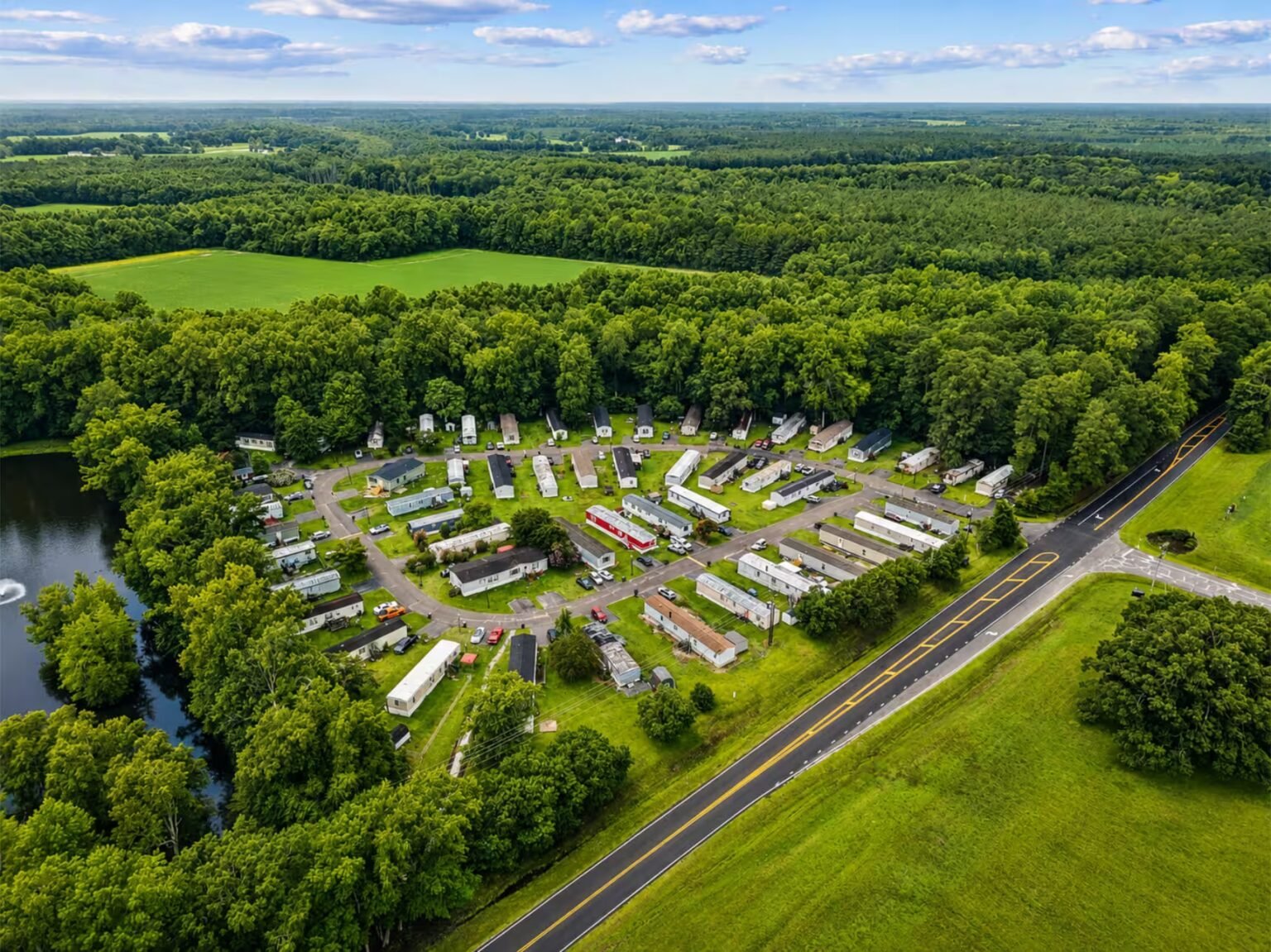 Aerial view of an RV campground with rows of white trailers surrounded by lush green forest.