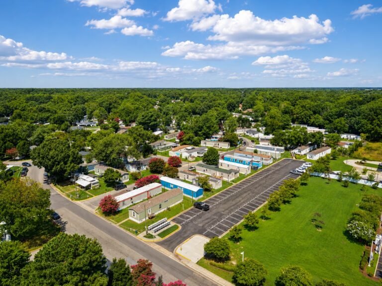 Aerial view of suburban homes along winding tree-lined streets under a bright partly cloudy sky.