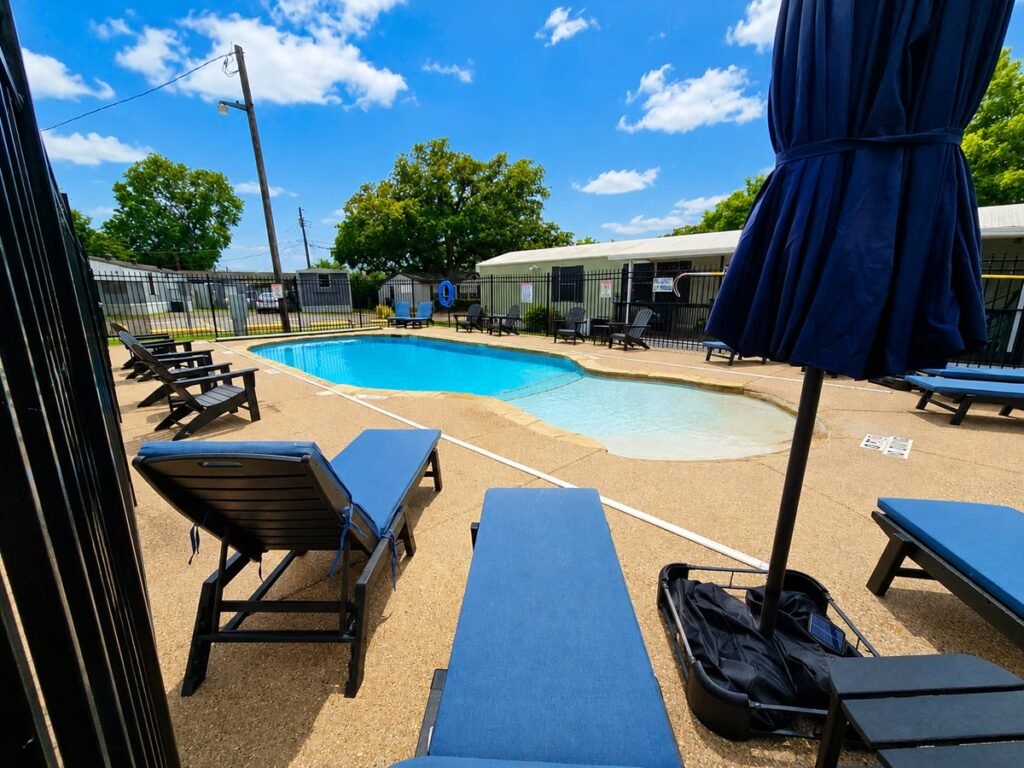Resort swimming pool surrounded by lounge chairs beneath blue shade umbrellas on a sunny day.