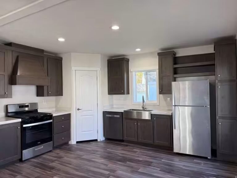 Dark wood kitchen cabinets, stainless steel refrigerator and range, light flooring in bright room.