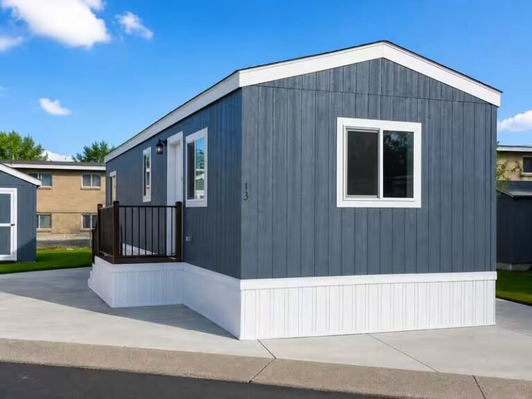 Blue single-wide manufactured home with white trim parked on paved lot beneath partly cloudy sky