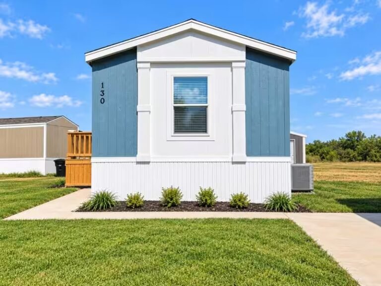 Blue and white manufactured home with front porch on a grassy lot under a partly cloudy sky.