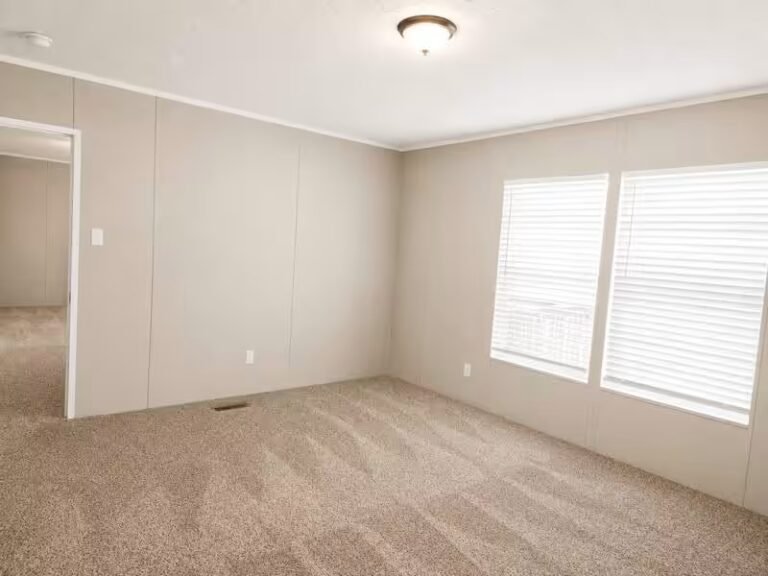 Empty carpeted room with beige walls, two windows with white blinds, a doorway, and ceiling light.