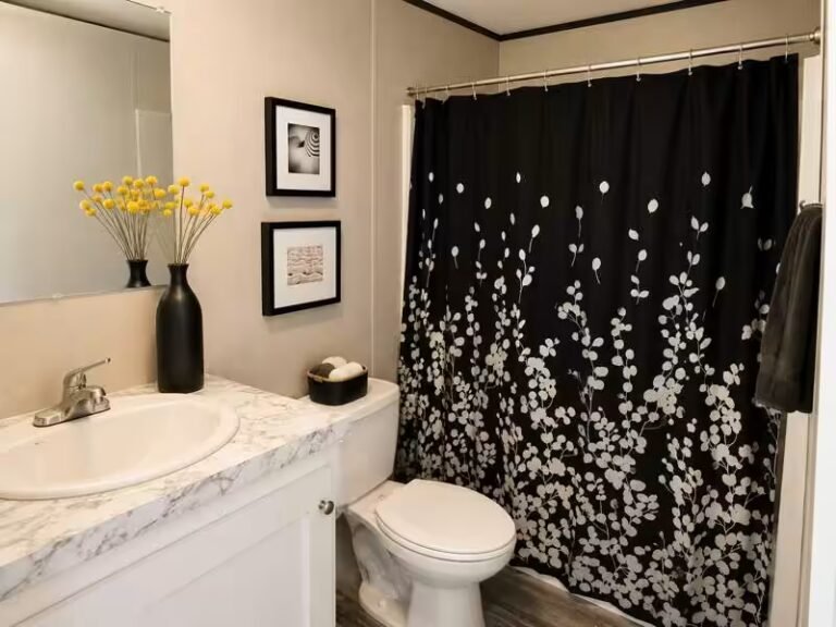 Bathroom corner with white vanity and sink beside a black-and-white floral shower curtain over a toilet.