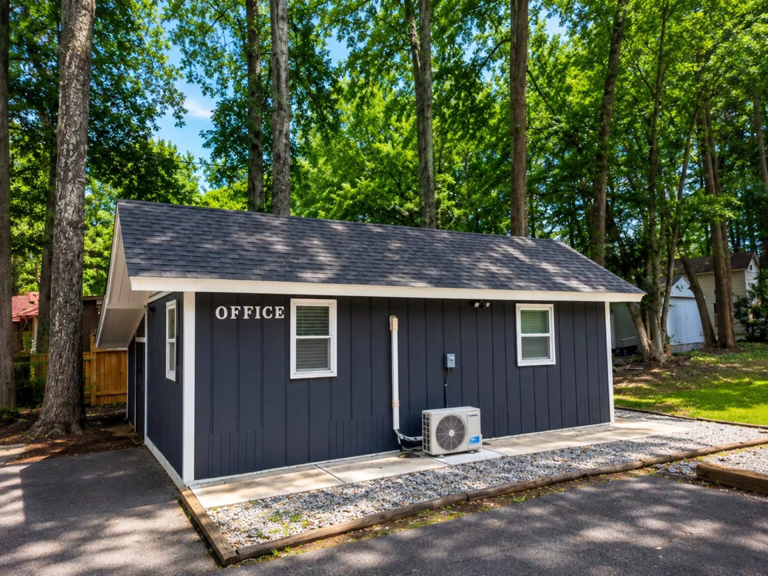Small navy-blue cottage with white trim nestled among tall green trees on a sunny day.